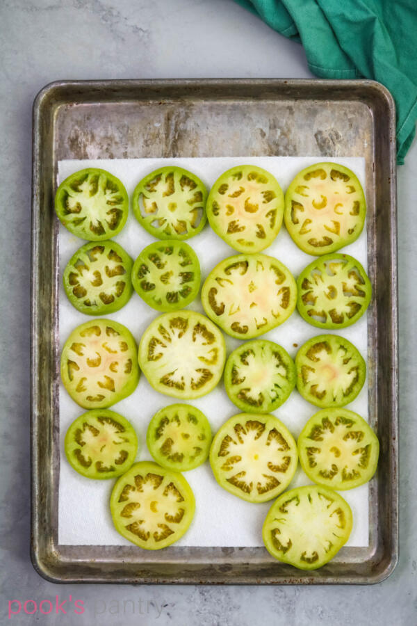 Slices of green tomatoes on paper towel-lined baking sheet.