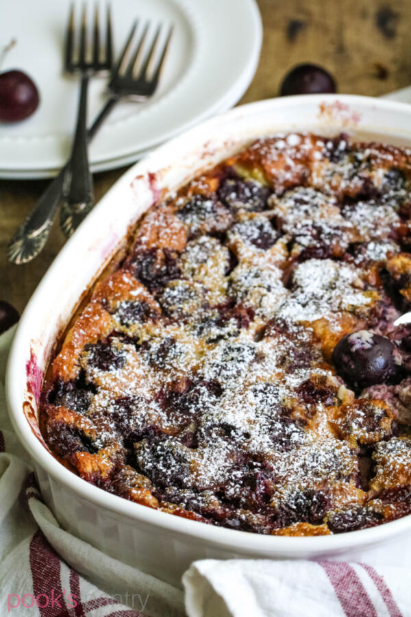 Cherry clafouti in white baking dish with fresh cherries in background.