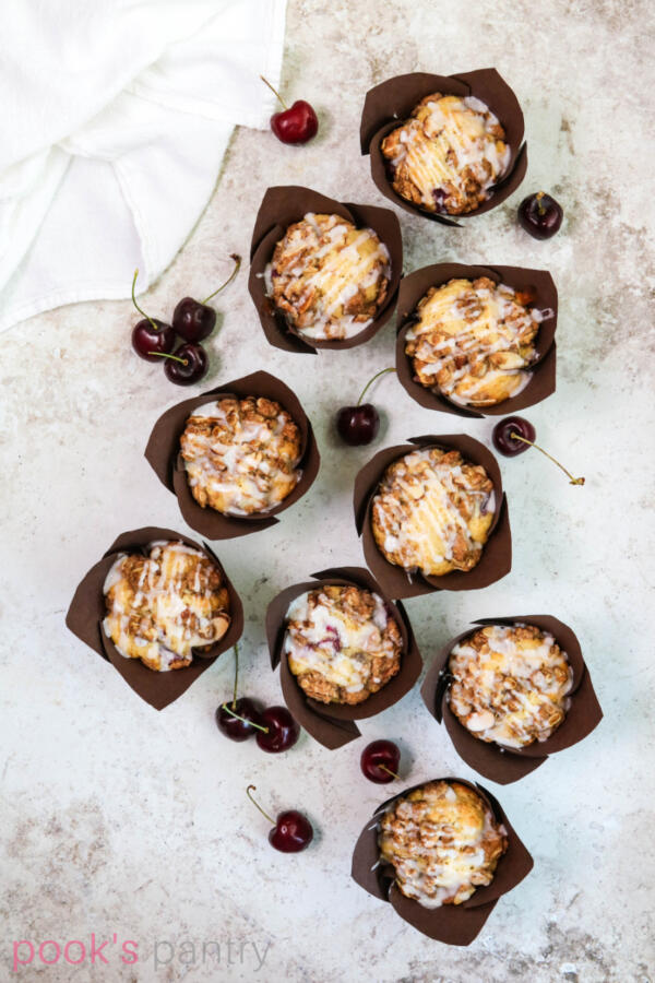 Fresh cherry muffins in tulip paper liners with cherries scattered in the background.