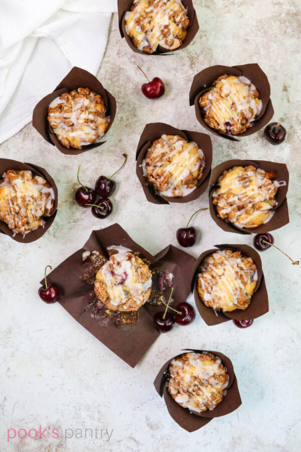 Overhead shot of muffins with fresh cherries and cinnamon streusel topping on tan background.