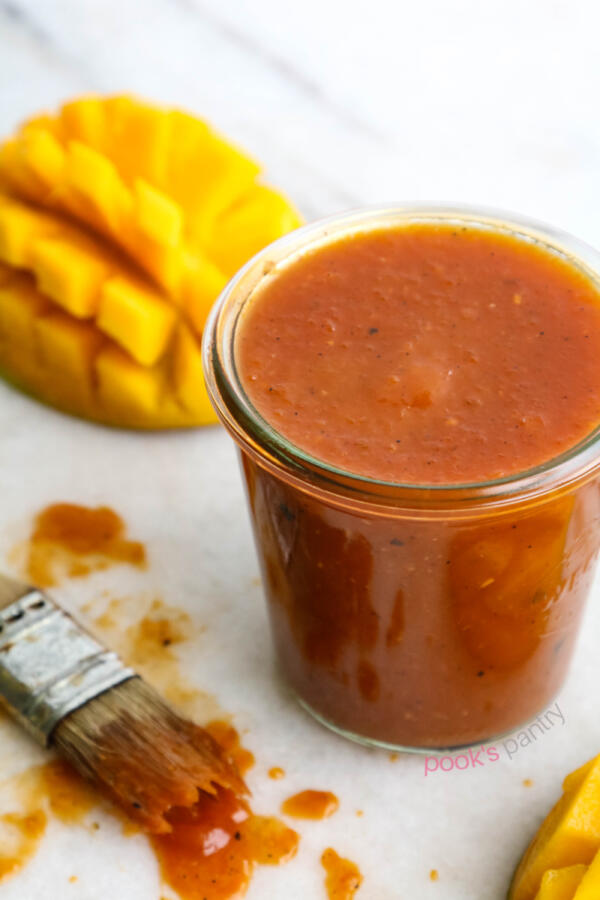 Mango pineapple BBQ sauce in glass jar with cut mangoes and brush on the side.