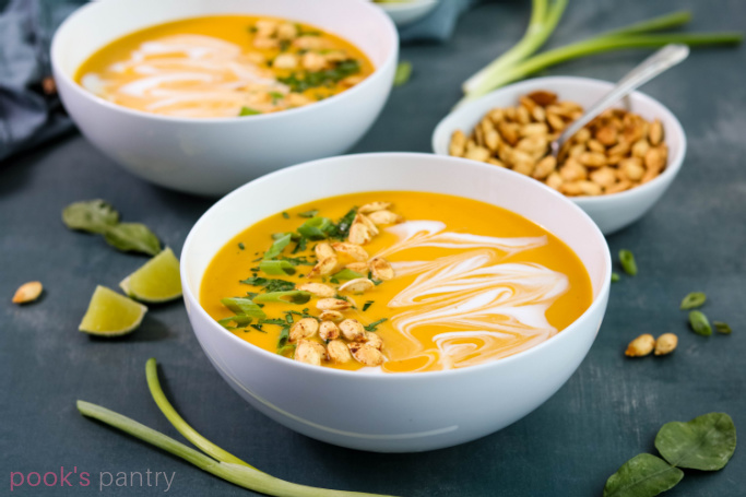 Bowls of curried squash soup with a small bowl of roasted Hubbard squash seeds on the side.