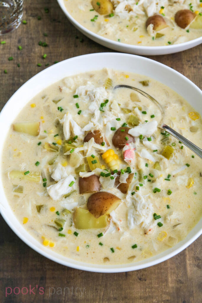 Overhead photo of bowl of chowder with fresh corn and crab meat on wooden table.