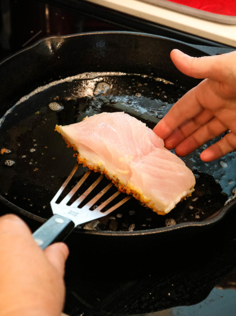 Flipping pan fried corvina fish in cast iron pan.