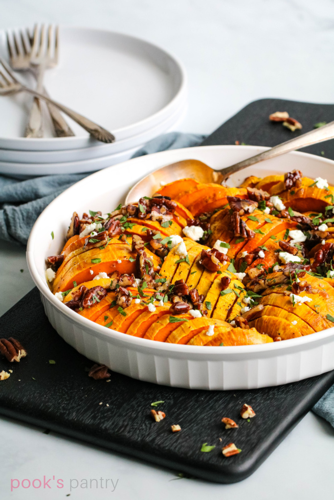 Roasted Honeynut squash with pecans and goat cheese in white casserole dish on black board.