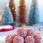 Peppermint rum balls on a white plate with bottle brush trees in the background.