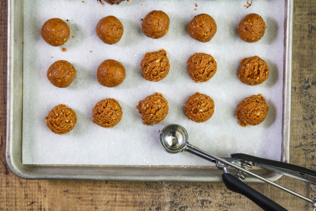 Scooping cookie balls with scoop on baking sheet.