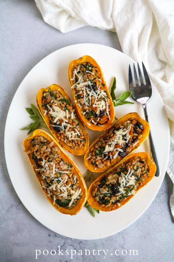 Stuffed delicata squash on white platter with herbs.