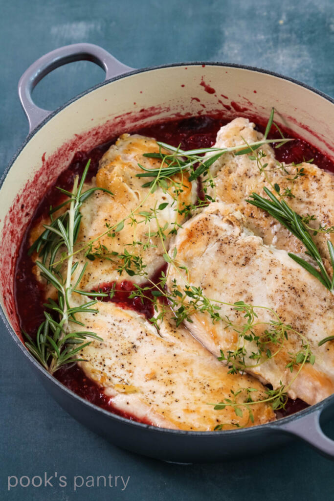 Cranberry chicken in pot with herbs.