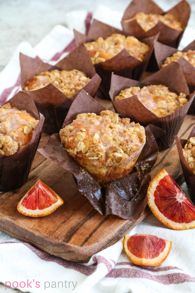 Orange muffins with crumble topping on brown wooden board.