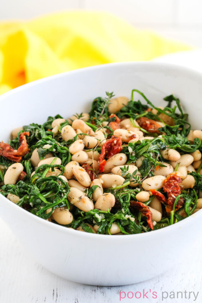 White beans and arugula with sundried tomatoes and garlic in a bowl.