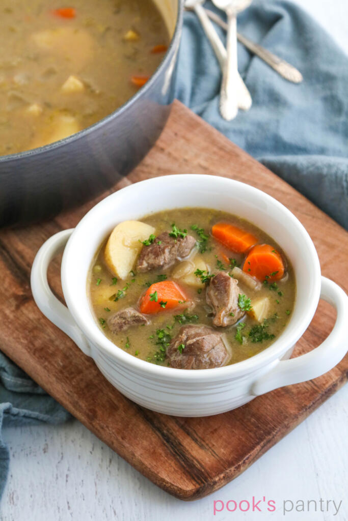 Irish lamb stew in white bowl on top of a wooden board with a grayish blue napkin.