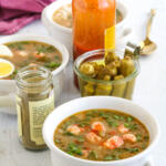 Langostino gumbo in white soup crocks with pickled okra and hot sauce in the background.