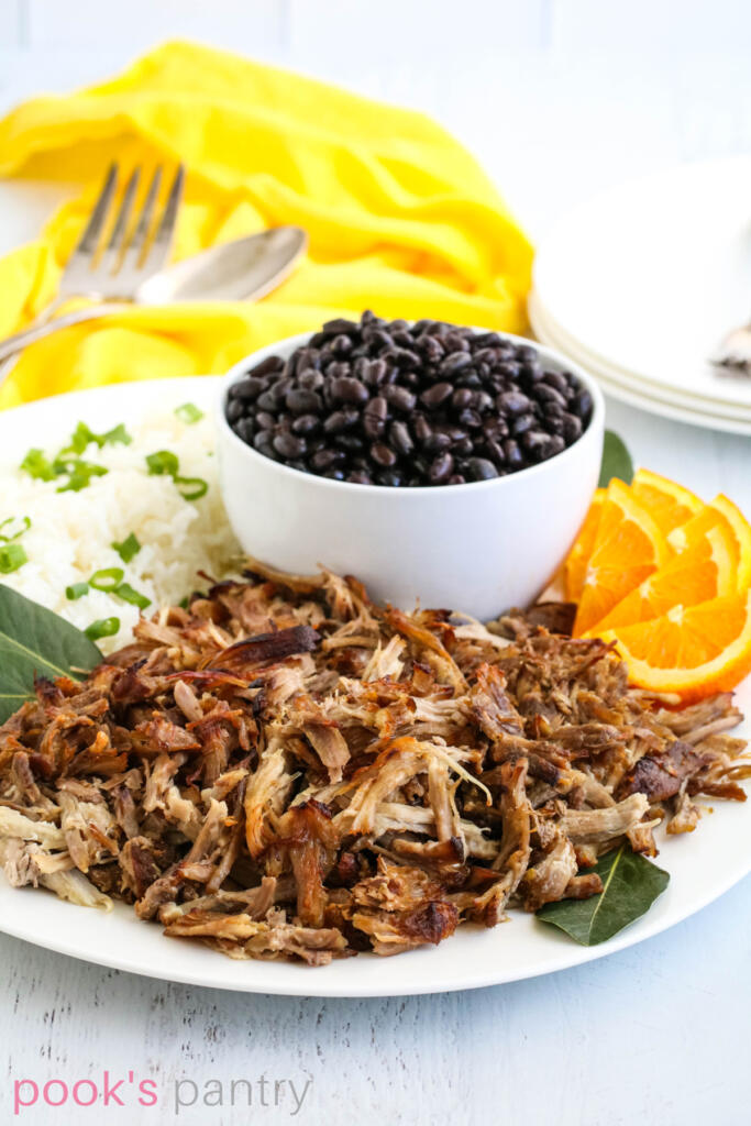 Orange pulled pork with garlic on white platter with black beans and rice.