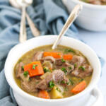 A bowl of Irish lamb stew with a silver spoon sitting on a blue napkin.