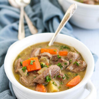 A bowl of Irish lamb stew with a silver spoon sitting on a blue napkin.