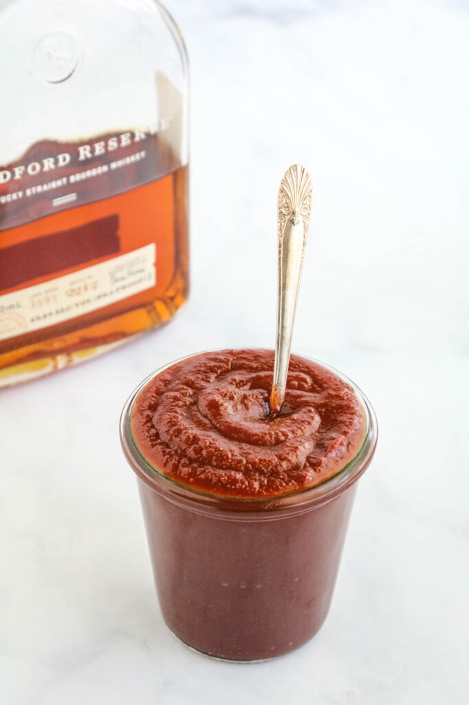 BBQ sauce in glass jar with bottle of bourbon in background.