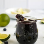 Blueberry lime jam in a Weck jar with blueberries and lime wedges in front.