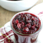 Cherry chutney in a glass jar with fresh cherries on the side.