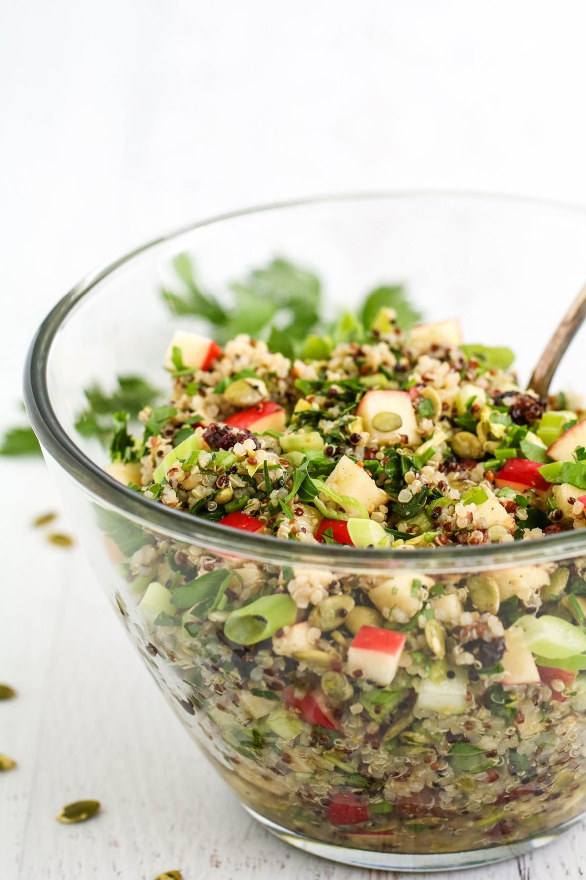 Apple quinoa salad with cranberries and pepitas in glass bowl.