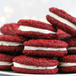 Red velvet sandwich cookies stacked on a white platter.