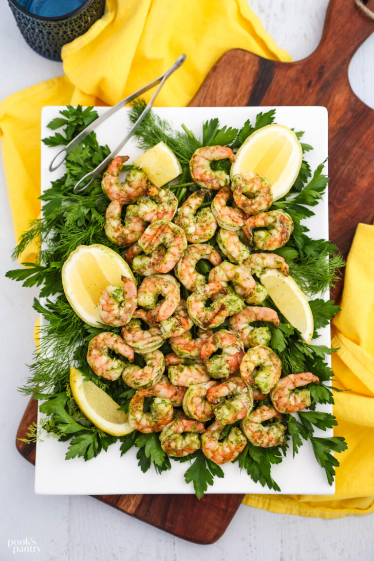 Grilled lemon herb shrimp on a white platter with herbs and lemon wedges.