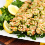 Gremolata shrimp on a white platter with herbs, sitting on a brown wooden board.