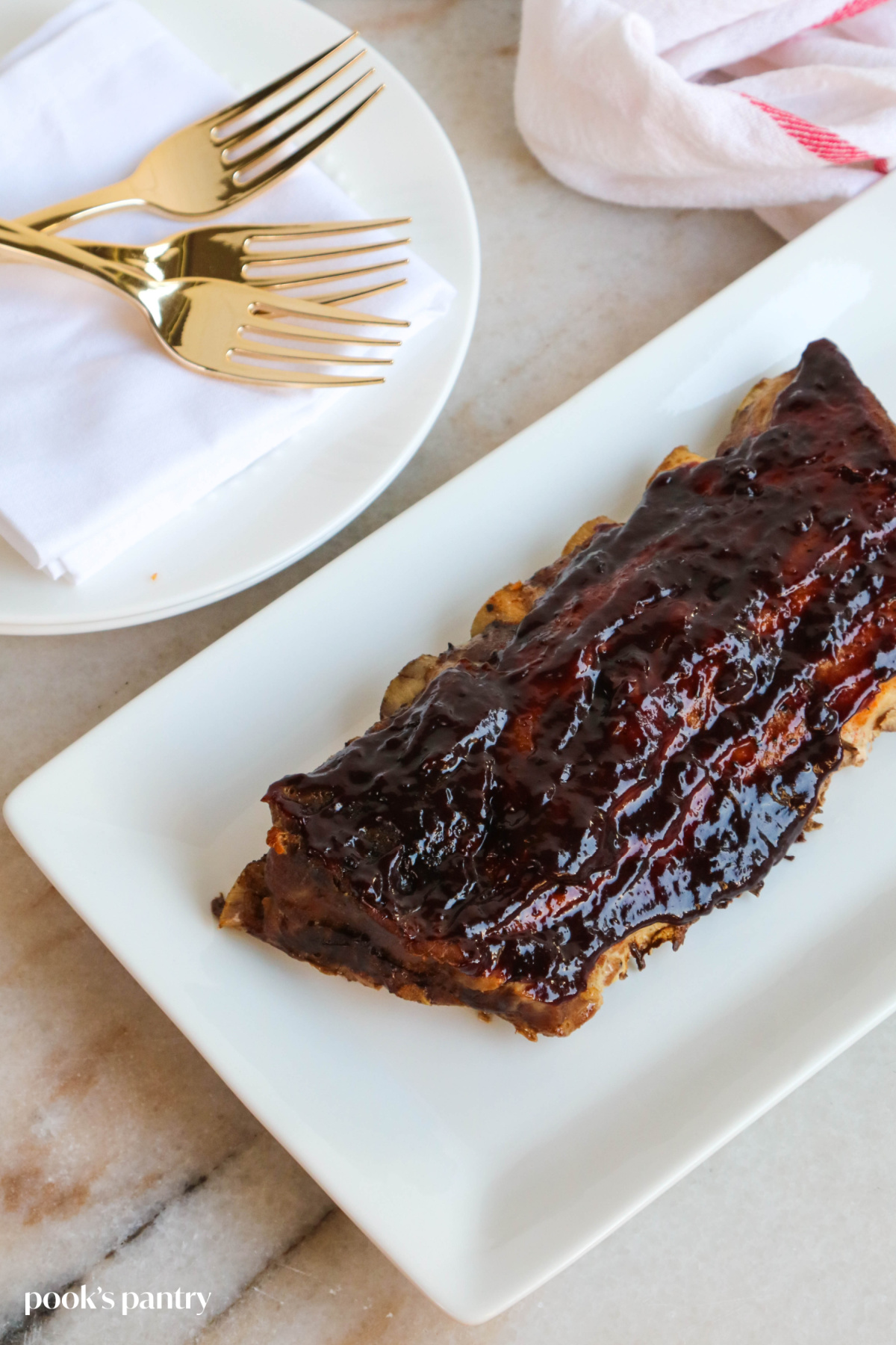Baby back ribs slathered in blueberry BBQ sauce on a white platter, with a stack of plates behind the ribs.