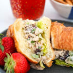 Apple cranberry chicken salad on a croissant, on a black plate.