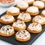 Soft pumpkin cookies with cinnamon frosting and sprinkles on a black wooden board.