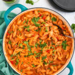 Cheesy chicken taco pasta recipe in a wide, shallow teal pan with a blue green towel next to the pan.