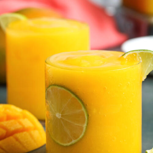 Frozen mango daiquiri in clear rocks glass with a slice of lime.