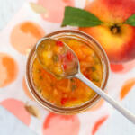 Peach pepper jam in a glass jar with a spoon resting on top.