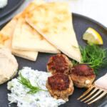 Mediterranean lamb meatballs with hummus, pita and tzatziki on black plate.