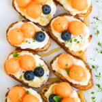 Pieces of melon bruschetta with herbs and honey on a white platter.