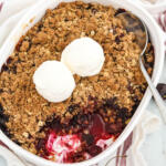 Cherry crisp with scoops of vanilla ice cream in casserole dish with spoon.