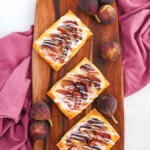 Fig puff pastry tarts on a wooden cutting board with a purple towel underneath it. There are clusters of figs around the board.