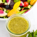 Lemon basil vinaigrette in glass jar with a bowl of salad behind it.