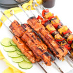 Teriyaki salmon skewers with skewered pineapple and slices of lime on white oval platter.
