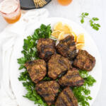 Overhead photo of a grilled lamb chops recipe. The lamb is seasoned with Middle Eastern spices, and it is on a white platter with herbs and lemon.