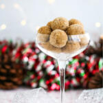 Rumchata balls in tall coupe glass on a white background with Christmas decorations behind the glass.