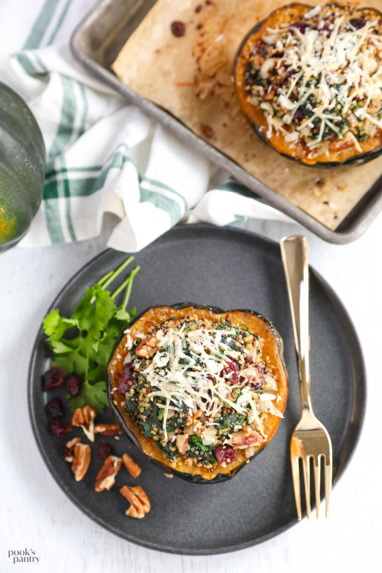 Vegetarian stuffed acorn squash on a black plate with pecans and cranberries on the side.