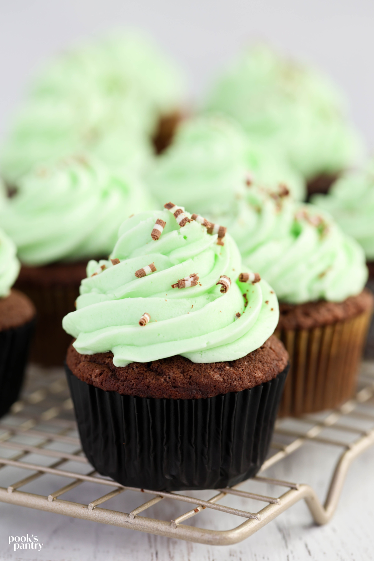 Frosted cupcakes on a metal cooling rack against an off-white background.