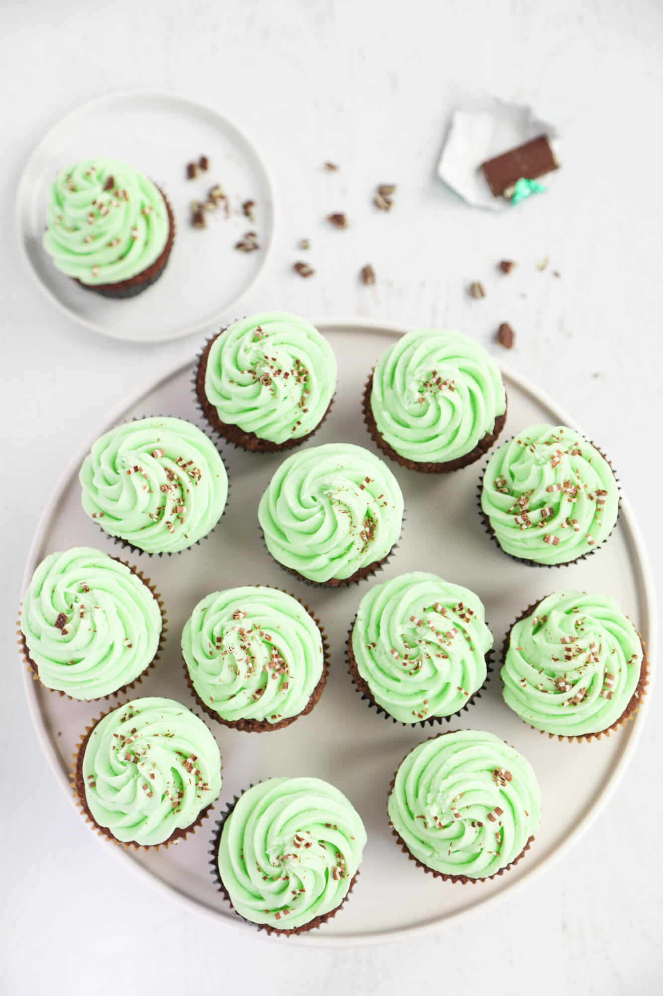 Thin mint cupcakes on a white cake stand with chocolate mint candies scattered on the background.
