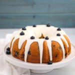 Blueberry Bundt cake on a cake stand, with glaze and blueberries on top.