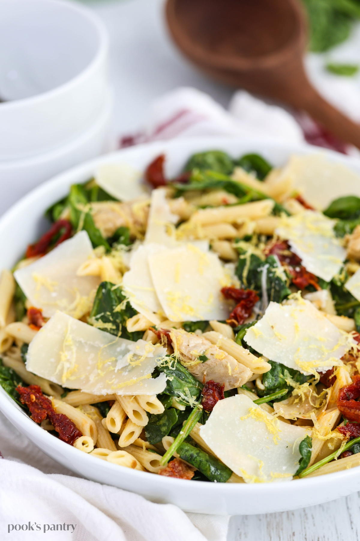 Pasta salad served in a large white bowl, topped with shaved parmesan and lemon zest.