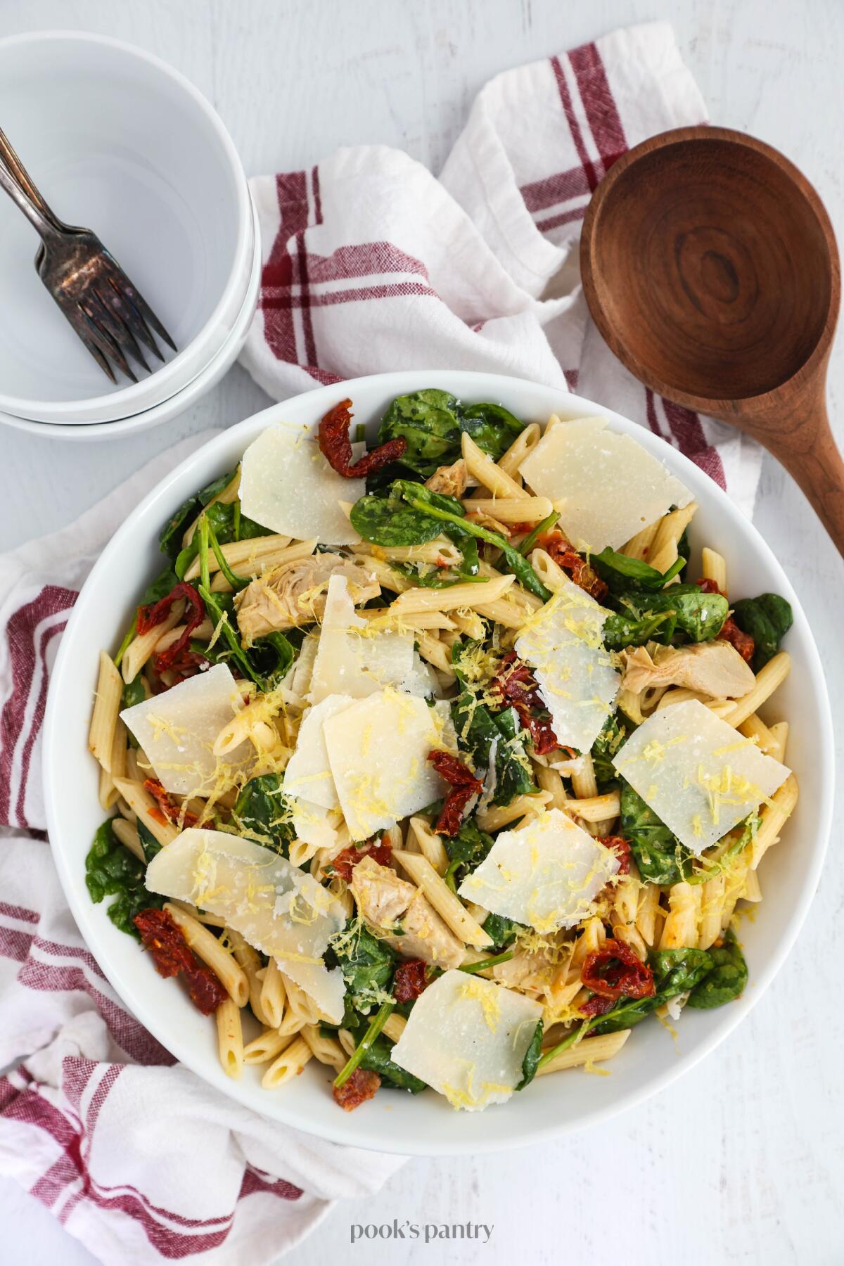Pasta salad served in a large white bowl, topped with shaved parmesan and lemon zest.