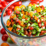 Israeli salad in glass bowl with tomatoes and cucumber in the background.