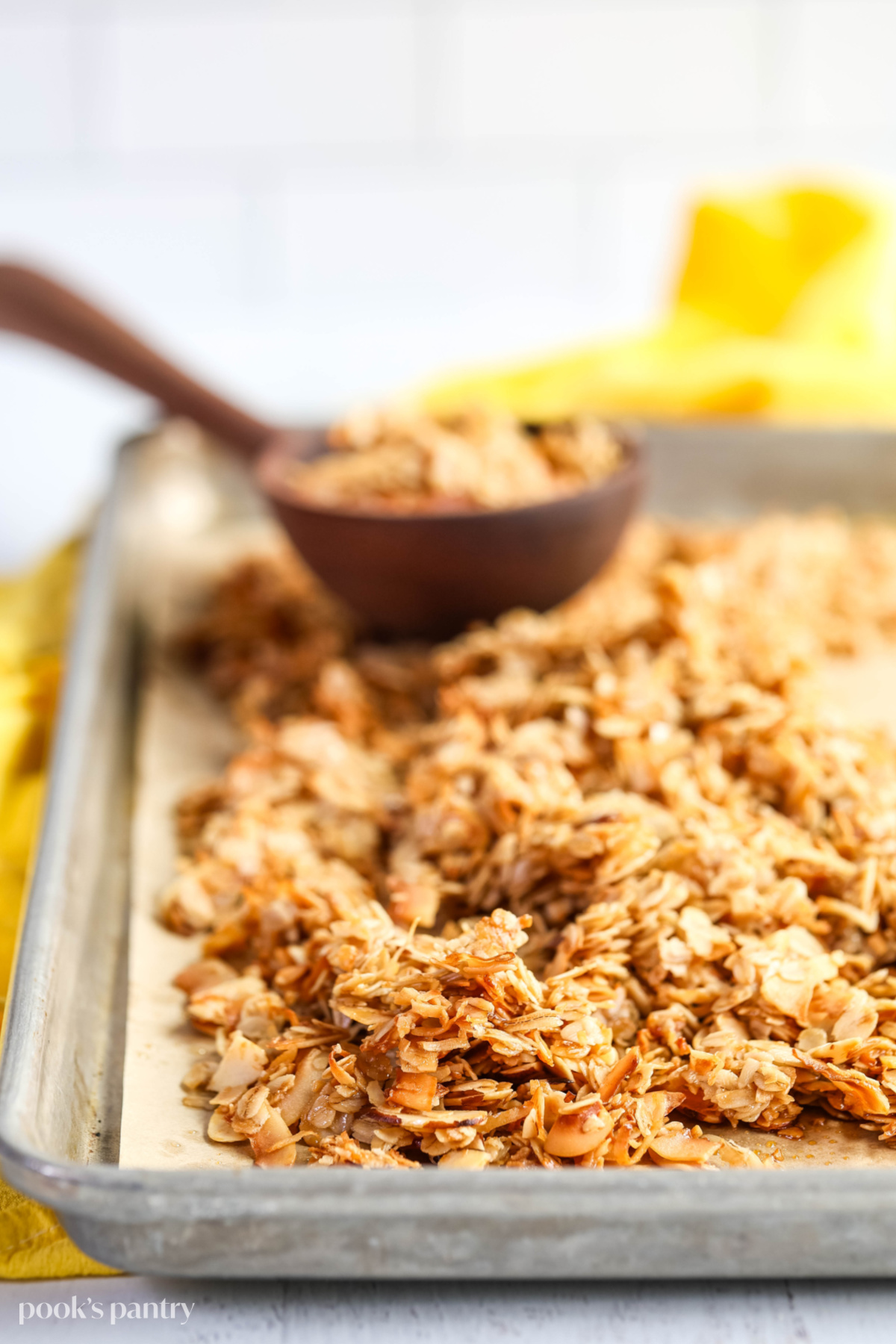 Coconut granola on a sheet pan with a wooden ladle full of granola in the background.