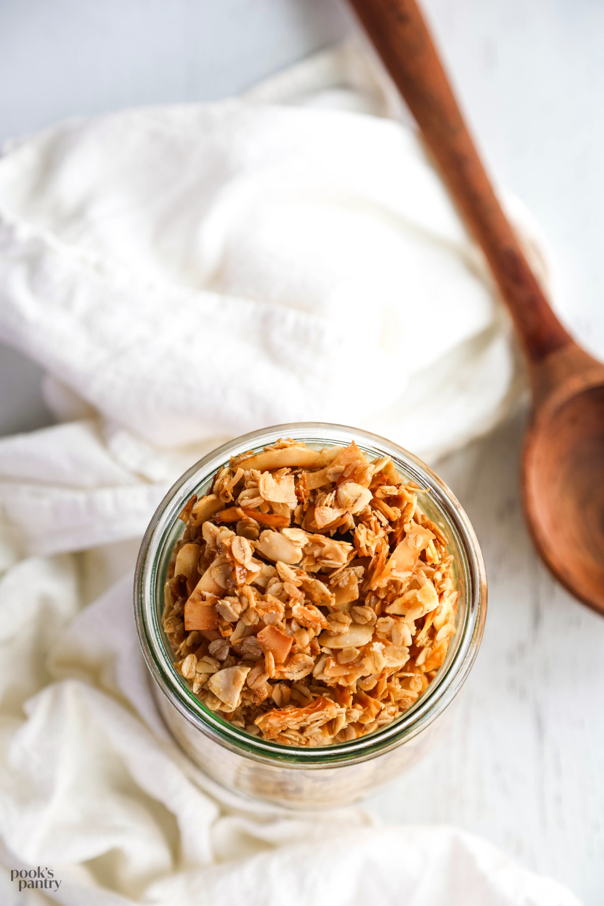 A glass jar filled with granola sitting on a white tea towel.
